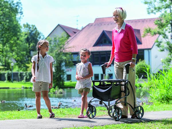 Ältere Frau mit Rollator geht mit zwei Kindern im Park spazieren